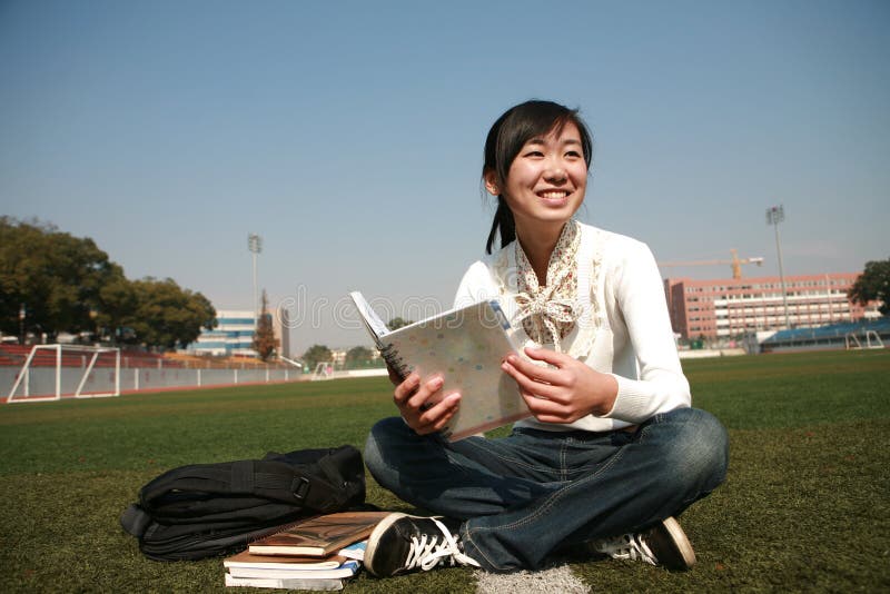 Girl holding books sitting on grasslan