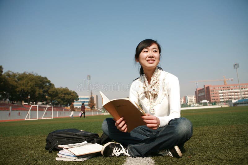 Girl holding books sitting on grasslan