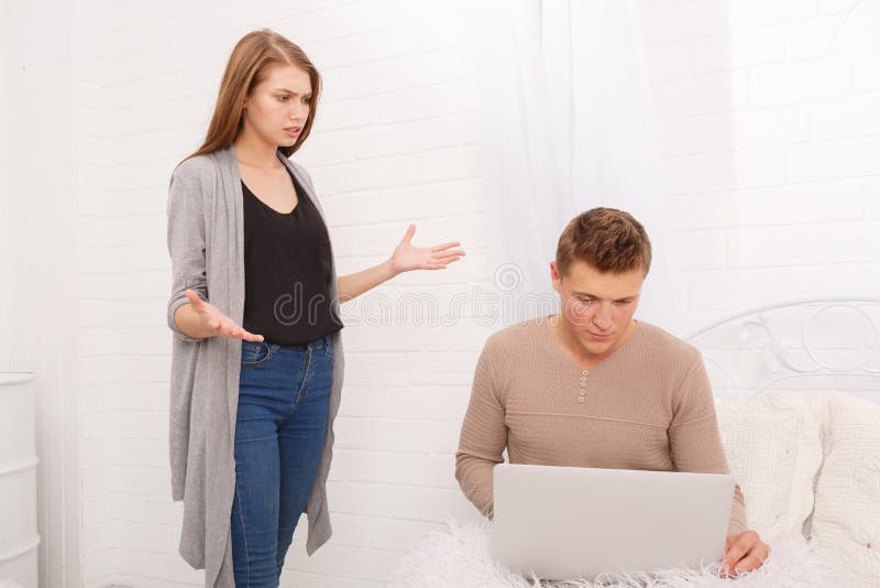 A girl is holding hands with a guy standing with a laptop on the bed