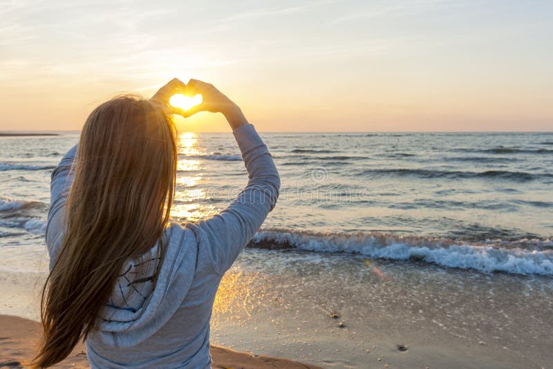 Girl holding hands in heart shape at beach