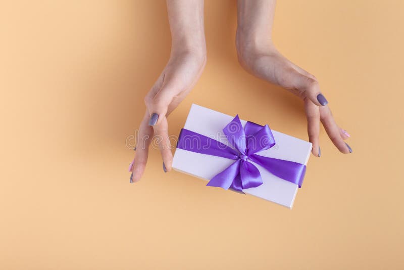 Girl holding a present in hands, women with gift box with a tied lilac ribb...