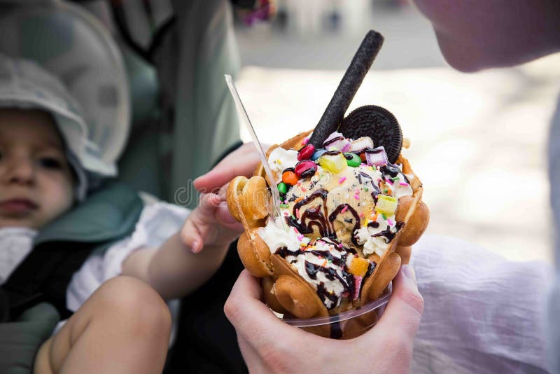 A girl holds a Hong Kong waffle dessert in her hand. Sweets with ice cream, cookies, syrup and sweets. Against the background, the