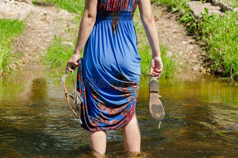 Girl holds sandals wade barefoot flowing stream