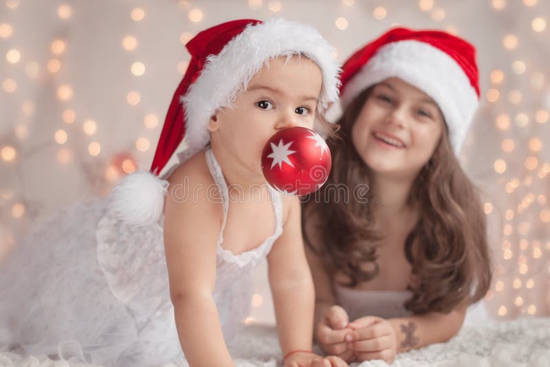 Girl hugs her little sister, both wearing red Christmas caps and royalty free stock image Girl hugs her little sister, both wearing red Christmas caps and royalty free stock image