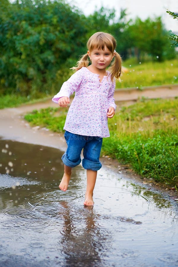 Girl junps barefoot in a puddle splashing water in the rain