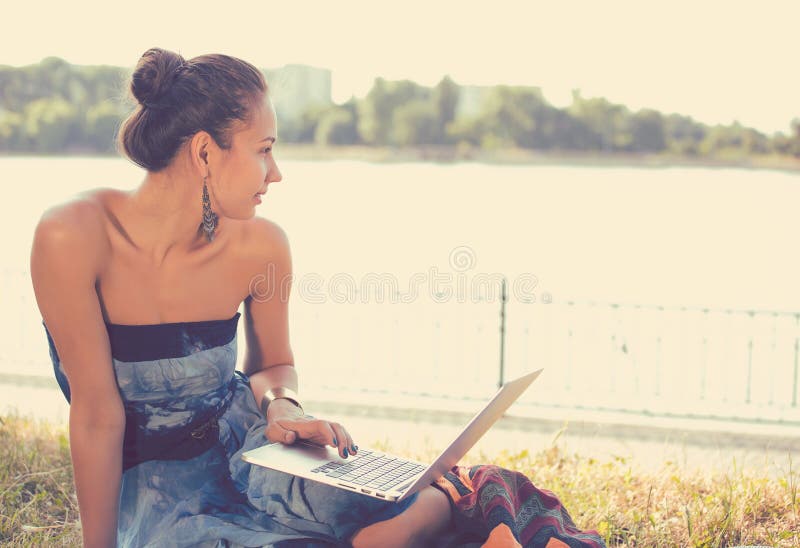 Girl with laptop. Beautiful woman with notebook sitting on the grass