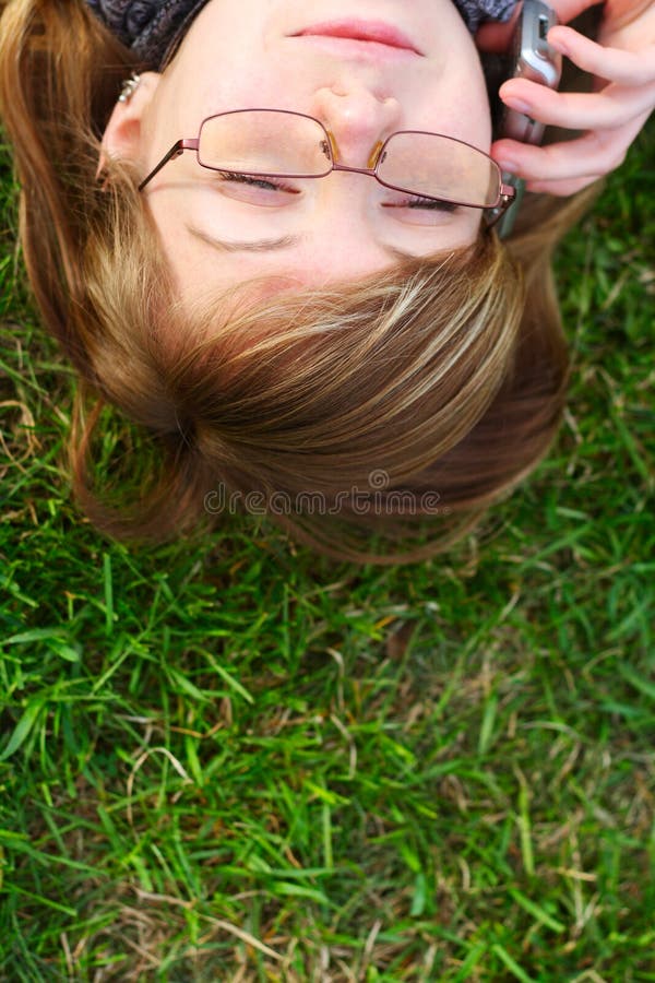 The girl lays on a grass with phone