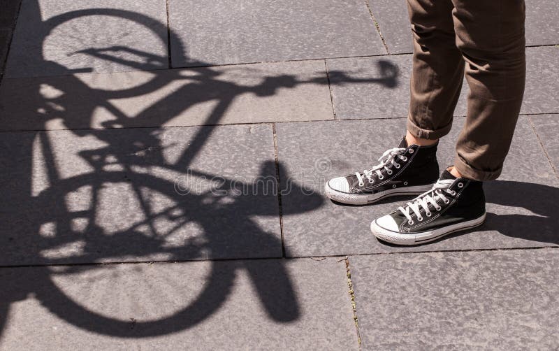 Girl legs wearing black snickers and skinny brown trousers in front of the shadow of a bicycle