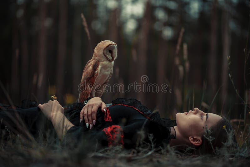 Girl lies with owl on grass in forest.