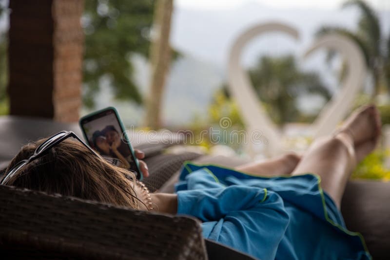 The girl lies on a sun lounger by the pool and looks at photos in a smartphone. in the background a heart in blur. selective focus
