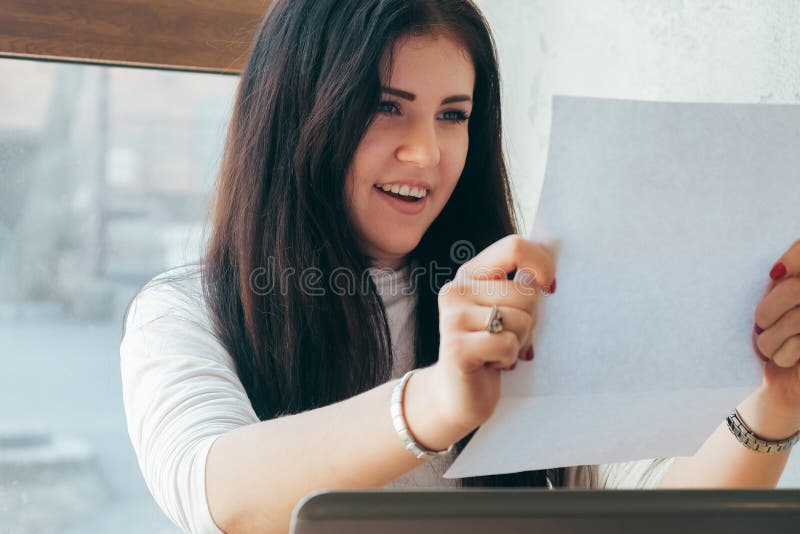 The girl in light clothes on a gray background is looking at documents and smiling. Coworking at home, work in a cafe royalty free stock photos The girl in light clothes on a gray background is looking at documents and smiling. Coworking at home, work in a cafe royalty free stock photos