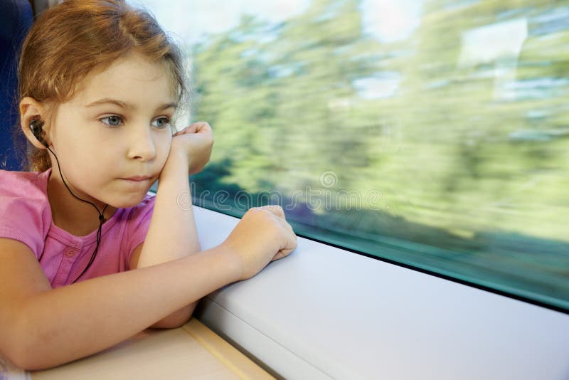 Girl listens to music, sitting by window of train