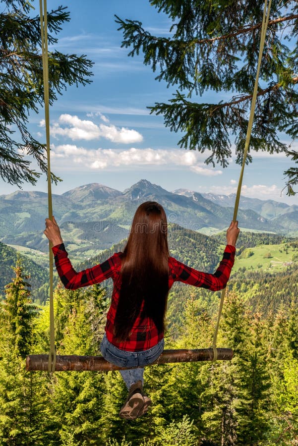 Girl with long hair swinging on forest swing with beautiful mountain view