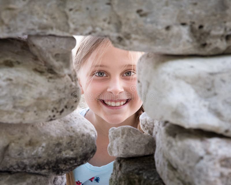 Girl Looking at Camera Through Hole in a Rock Wall