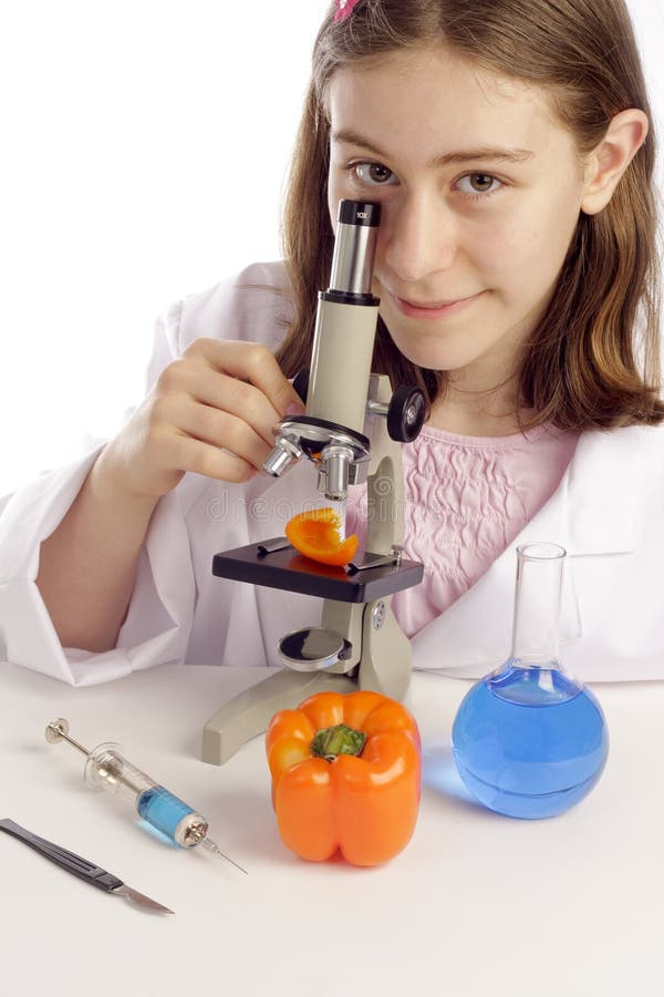 Young girl is using microscope to look at a bright orange pepper with a microscope. She has a flask of blue liquid and a syringe full of blue liquid. Young girl is using microscope to look at a bright orange pepper with a microscope. She has a flask of blue liquid and a syringe full of blue liquid.