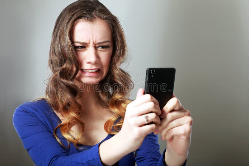 Closeup portrait anxious scared young girl looking at phone seeing bad news photos message with disgusting emotion on her face isolated on gray wall background. Human reaction