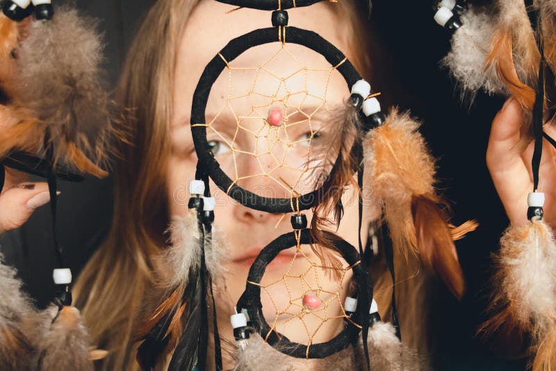 The girl looks through the catcher`s ring of dreams with her beautiful and wide-open eyes. With her hands she holds feathers that hang from the catcher dreams royalty free stock images