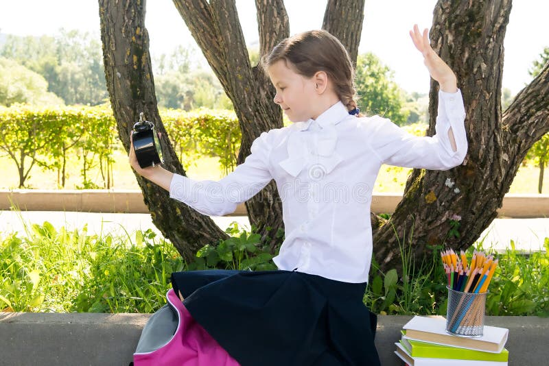 Girl looks surprised at the clock in the summer outside, it`s time to go to school stock photos Girl looks surprised at the clock in the summer outside, it`s time to go to school stock photos