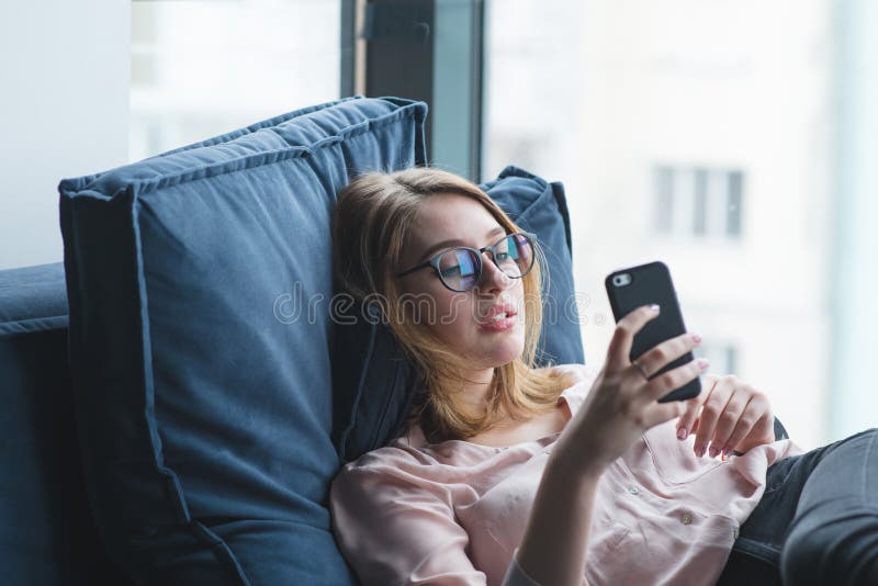 Girl lying on the couch and using a smartphone. The girl is resting on the couch with a smartphone in her hands