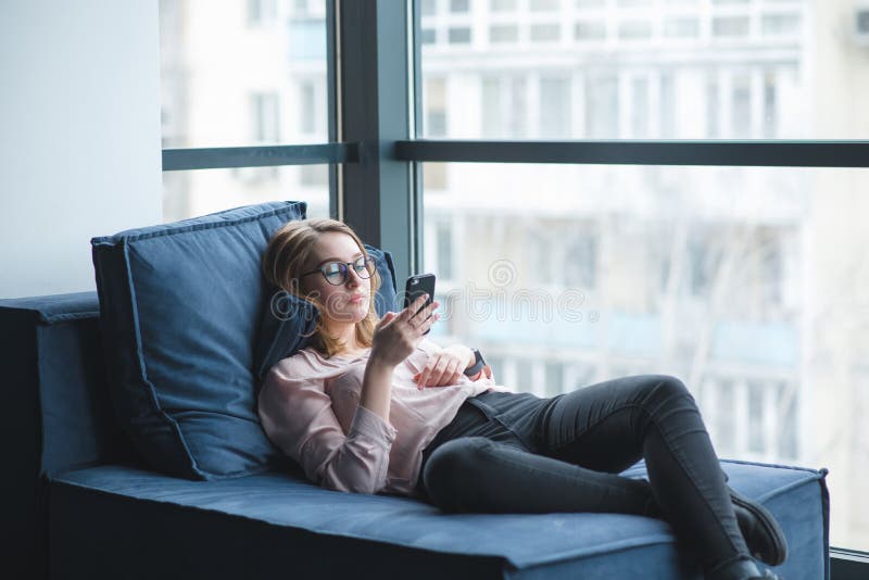 girl lying on the couch at the window and using a mobile phone