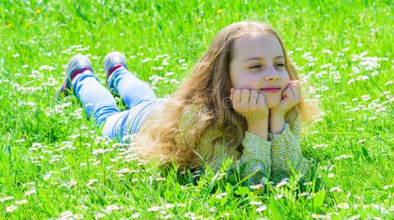 Girl lying on grass at grassplot, green background. Child enjoy spring sunny weather while lying at meadow. Springtime