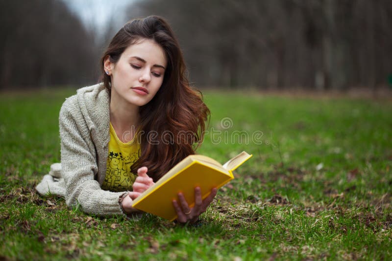 Girl lying in a grass and reading book