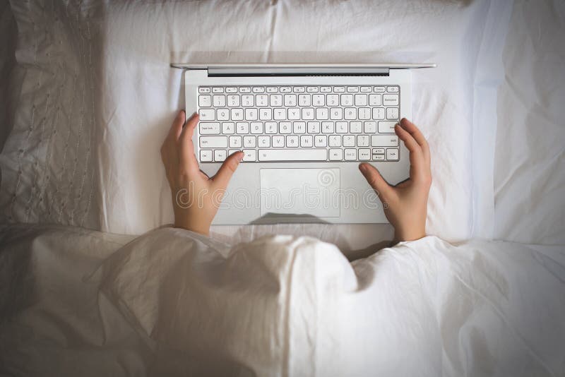 Girl lying with a laptop in bed covered by blanket. Woman can`t sleep and have to work late at night.