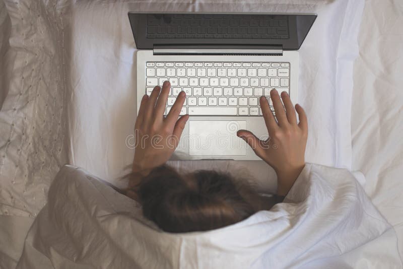 Girl lying with a laptop in bed covered by blanket. Woman can`t sleep and have to work late at night.