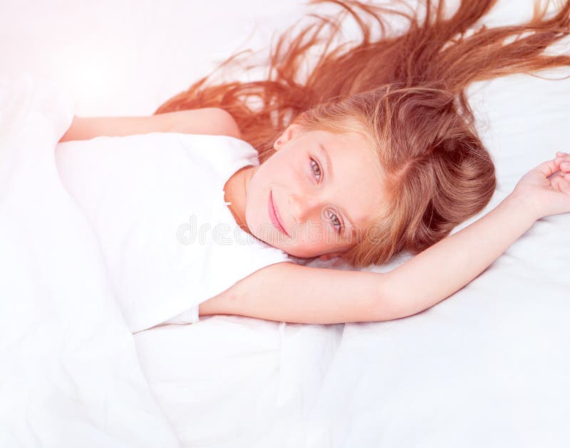 Bella bambina di sei anni che giace in un letto bianco con il suo orsacchiotto di peluche.