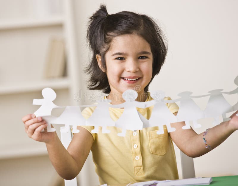 Mladá dívka sedí u stolu a drží papírové panenky.