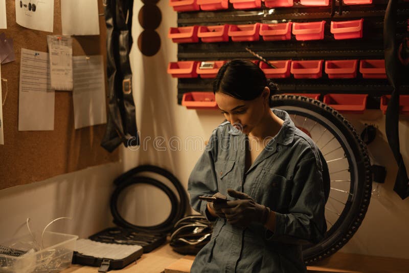Girl mechanic repairing a bike in a workshop or garage using a smartphone to find the problem of a broken bicycle royalty free stock image