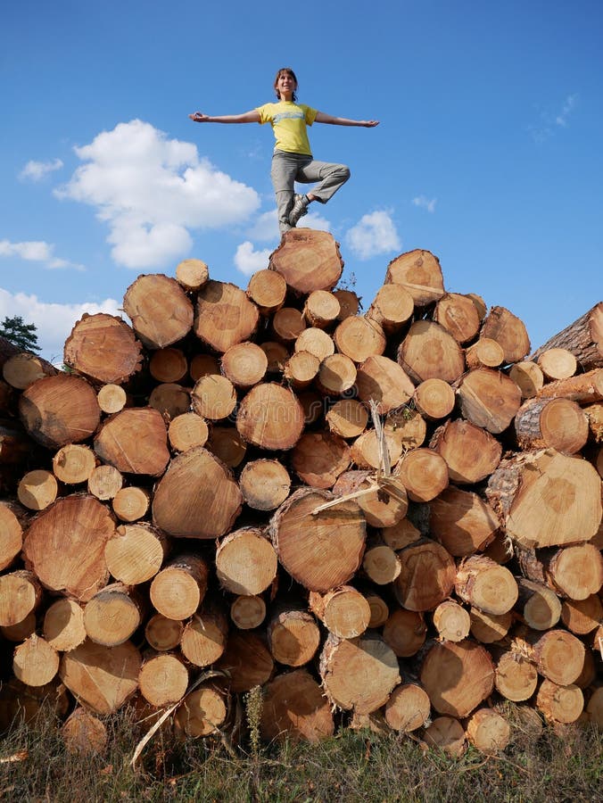 A girl meditates on one foot on top of a stack of logs royalty free stock photography