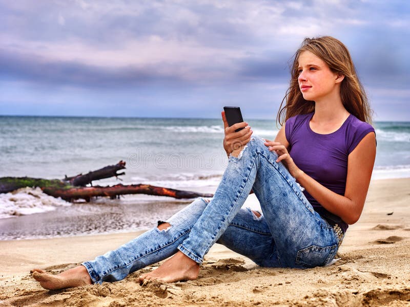 Girl with mobile phone sitting on sand near sea