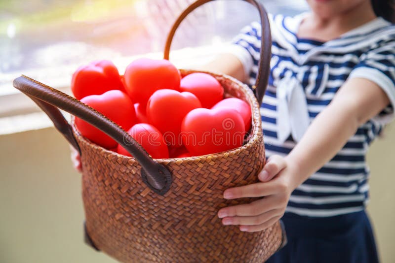 Girl in navy blue striped dress handing basket of red hearts represents helping hands, family support, morale, purity, innocence, royalty free stock photo Girl in navy blue striped dress handing basket of red hearts represents helping hands, family support, morale, purity, innocence, royalty free stock photo