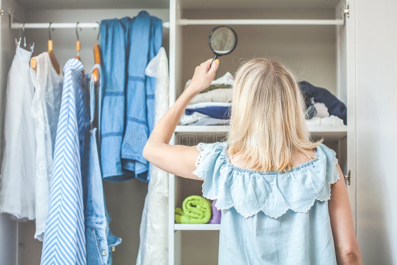 The girl near the wardrobe with clothes is looking with a magnifying glass that she should wear. Heavy Choice Concept nothing to w stock images The girl near the wardrobe with clothes is looking with a magnifying glass that she should wear. Heavy Choice Concept nothing to w stock images