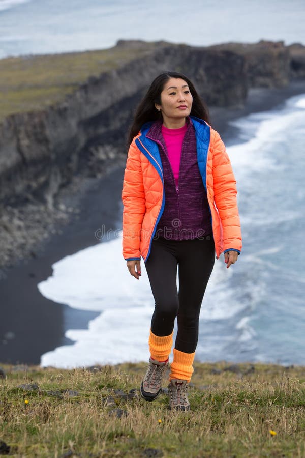 A girl in an orange jacket walks along a rocky ocean shore stretching to the horizon royalty free stock images A girl in an orange jacket walks along a rocky ocean shore stretching to the horizon royalty free stock images