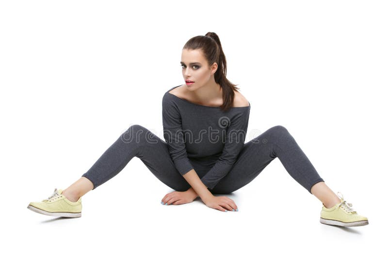 Beautiful young woman in grey overalls and yellow sport shoes with legs spread. Isolated over white background. Copy space. Beautiful young woman in grey overalls and yellow sport shoes with legs spread. Isolated over white background. Copy space.