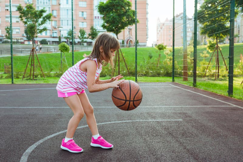 A girl on the playground with a ball plays basketball.  Outdoor city basketball court