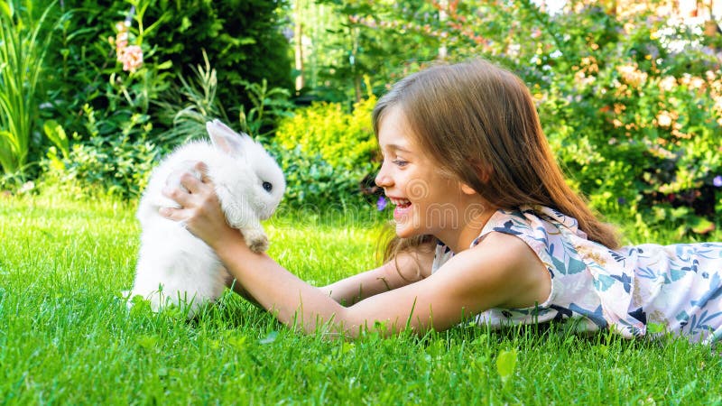 A girl is playing with a pet rabbit in the garden on the lawn. The concept of caring for nature and the animal world. stock photo