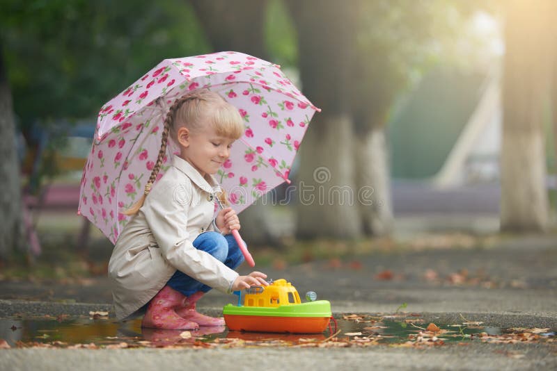 A girl playing in the puddle with the boat after rain stock image A girl playing in the puddle with the boat after rain stock image