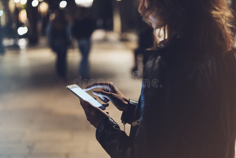Girl pointing finger on screen smartphone on background illumination bokeh color light in night atmospheric city, hipster using stock photography