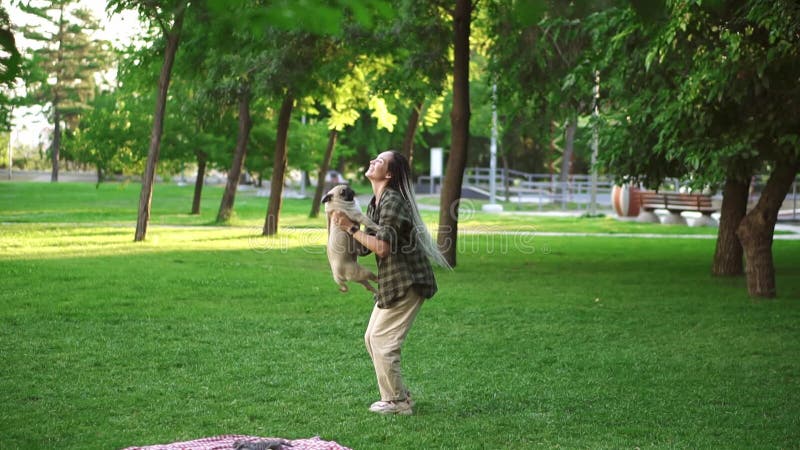 The girl and pug dog are having fun, she throws the dog in the air in the park stock video footage