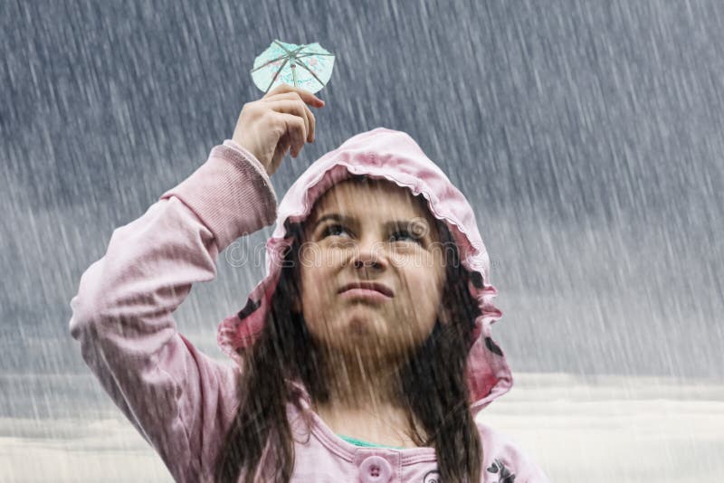 Una bambina in possesso di un cocktail di ombrello sotto la pioggia.