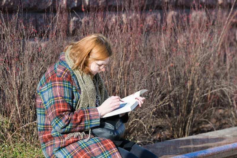 Girl is reading a book in the street. in the cold season. with red hair. in warm clothes stock photos Girl is reading a book in the street. in the cold season. with red hair. in warm clothes stock photos