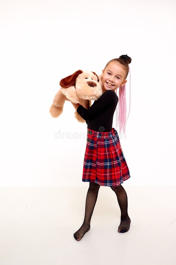Girl in in a red checked skirt and with toy dog in the studio with white background during photo shoot. Cute young
