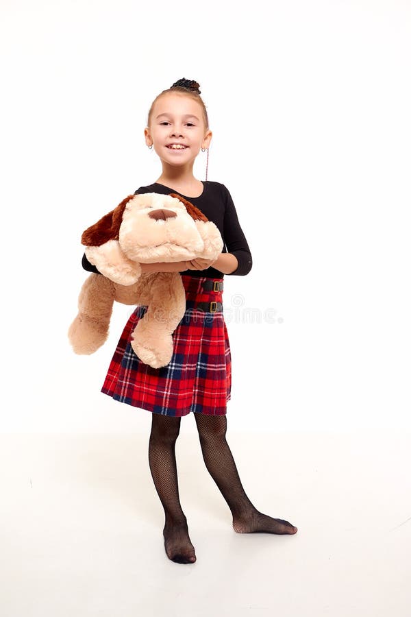 Girl in in a red checked skirt and with toy dog in the studio with white background during photo shoot. Cute young