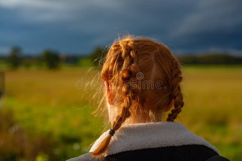 Girl With Red Hair in Braids Walks Through a Field in the Countryside