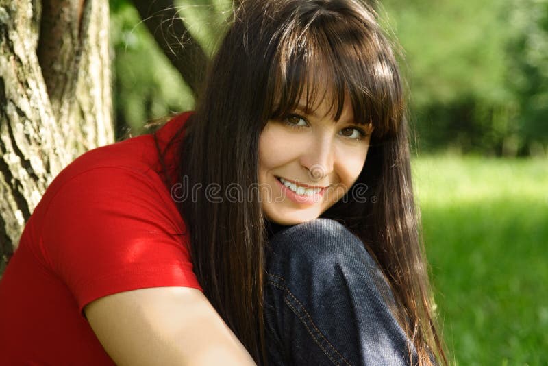 Girl in red shirt smiling and siting near tree