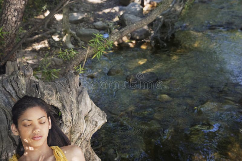 Girl Relaxing On Tree Trunk By Stream