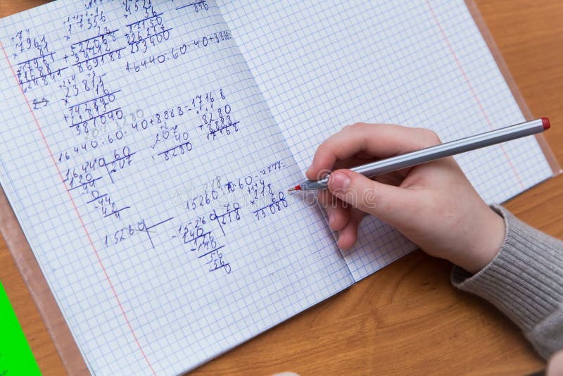 A girl& x27;s hand with a ballpoint pen close-up writes numbers in a notebook. stock image
